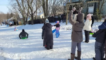 parents cheering their kids as the kids sled down a city street