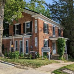 2 story brick home with a brick addition on the back in a wooded and rustic landscaped yard