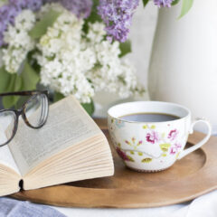 Open book, reading glasses, flowers, and cup of coffee
