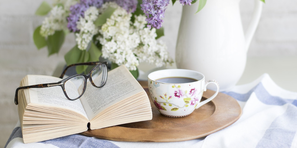 Open book, reading glasses, flowers, and cup of coffee