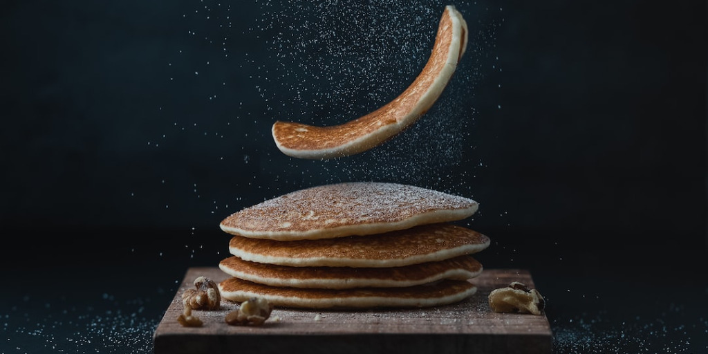 pancake being dropped on a stack of pancakes